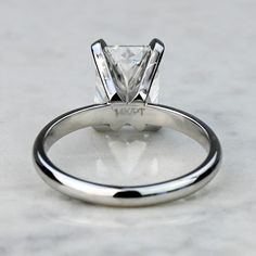 a white gold engagement ring with a princess cut diamond in the center, on a marble surface