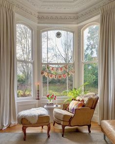 a living room filled with furniture next to two large windows covered in happy birthday decorations