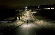 a person standing in the middle of an empty road at night with street lights on