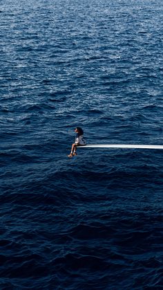 a person sitting on top of a boat in the middle of the ocean with their legs crossed