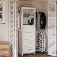 an open closet with white shutters and clothes hanging on the door, next to a small chest of drawers