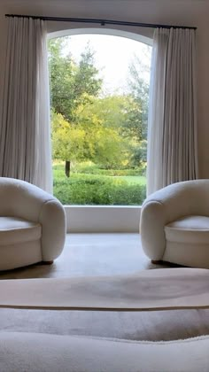 two white chairs sitting next to each other in front of a window with trees outside