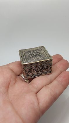 a hand holding a small metal box in it's left hand on a white surface