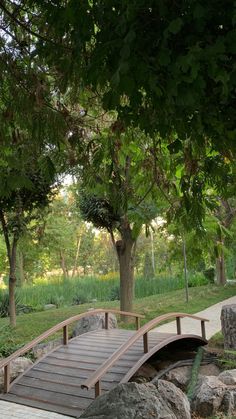 a wooden bridge over a small pond in a park with rocks and trees around it