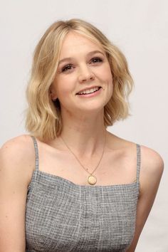 a woman with blonde hair wearing a gray top and gold necklace smiling at the camera