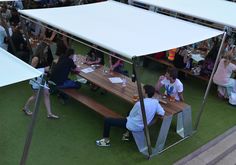 several people sitting at picnic tables under a tent with white canopy over them, while others sit on the grass