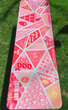 a pink snowboard with stickers on it sitting in the grass next to a tree