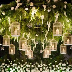 a bunch of birds in cages hanging from the ceiling with candles and flowers around them