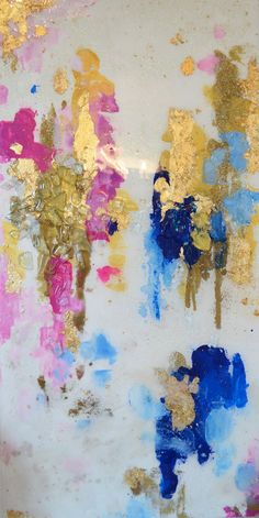 an abstract painting with gold, blue and pink paint splattered on the wall