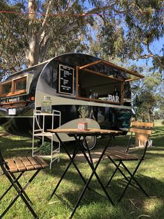 an rv is parked in the grass with two chairs around it and a table set up outside