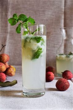 a glass filled with ice and mint on top of a table next to some fruit