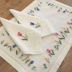 two napkins with flowers on them sitting on a wooden floor next to each other