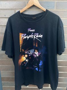 a black t - shirt hanging on a wall with the words prince of punk rain printed on it