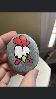 a hand holding a rock with a cartoon chicken painted on it