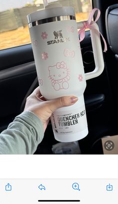 someone holding up a hello kitty tumbler cup in their car with pink bows on it