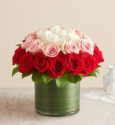 a green vase filled with red and white roses