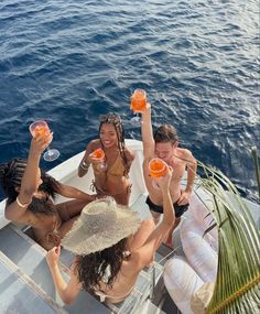 four people sitting on a boat with drinks in their hands and one person holding up two wine glasses