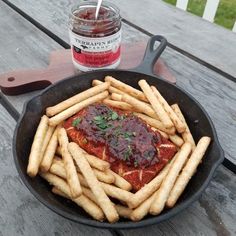 french fries and ketchup sit in a pan on a picnic table next to a jar of ketchup