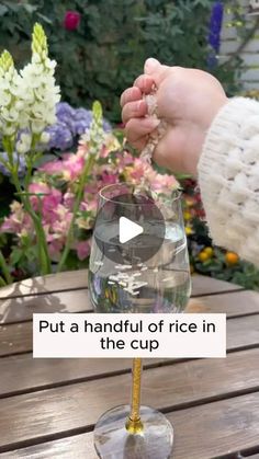 a person is pouring water into a wine glass on a table with flowers in the background