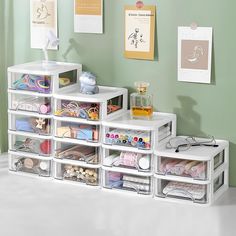 a white shelf filled with lots of crafting supplies on top of a floor next to a green wall