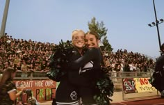 two women hugging each other in front of an audience at a sporting event, with one holding her arms around the other