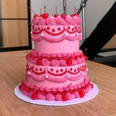 a three tiered cake with pink frosting and red icing hearts on it