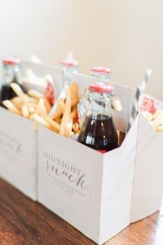 two bottles of soda and french fries in a white box on a wooden table next to each other