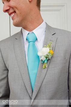 a man in a gray suit with a blue tie and flower boutonniere