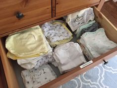 an open drawer filled with baby clothes on top of a rug