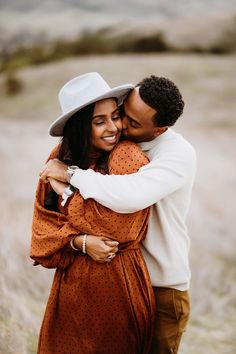 a man and woman hugging each other in the middle of a field