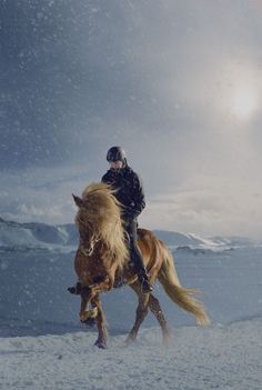 a man riding on the back of a brown horse in snow covered field next to mountains