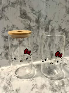 two hello kitty glasses sitting on top of a marble counter next to a wooden lid