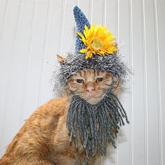 a cat wearing a hat with sunflowers on it's head, sitting next to a wall