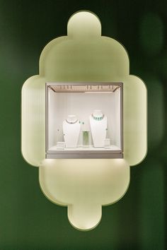 a green wall with two white vases in the middle and lights on each side