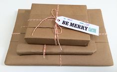 three brown wrapped presents tied with twine on white tablecloth and paper tag that says be merry