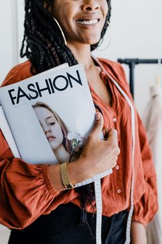 a woman with braids holding a fashion magazine in her right hand and smiling at the camera