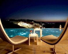 two chairs sitting next to each other near a swimming pool at night with the lights on