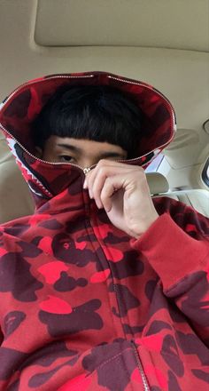 a young man wearing a red and black camouflage print hoodie in the back seat of a car