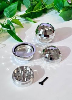 three shiny metal objects sitting on top of a white table next to green plants and leaves