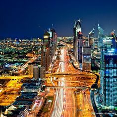 an aerial view of a city at night with cars driving on the road and buildings in the background