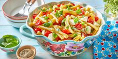 pasta salad with tomatoes, spinach and cheese in a bowl on a blue wooden table