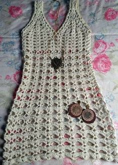 a white crocheted tank top with buttons on the front and bottom, laying on a bed