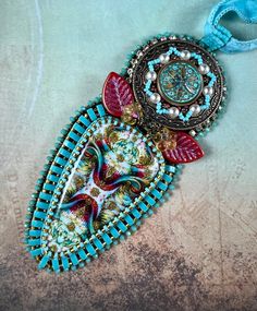 a blue and red necklace with an ornate design on it's side, hanging from a cord