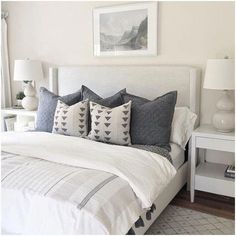 a bed with white sheets and gray pillows