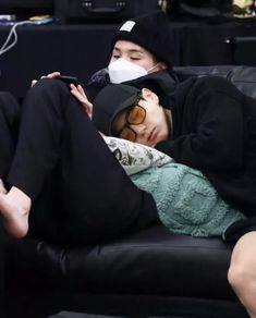 two people are sleeping on a couch wearing masks