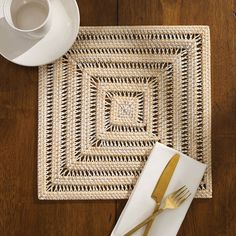 a placemat with a fork and knife on it next to a white cup, saucer and spoon