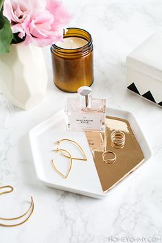 a white tray topped with gold jewelry next to a candle and pink flower on top of a table