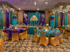 a banquet hall decorated with blue and purple balloons, gold tablecloths and chairs