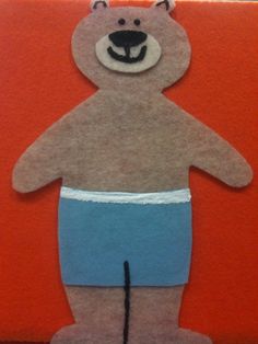 a paper cut out of a teddy bear wearing blue shorts and a diaper on an orange background