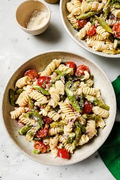 two bowls filled with pasta and vegetables on top of a white countertop next to green napkins